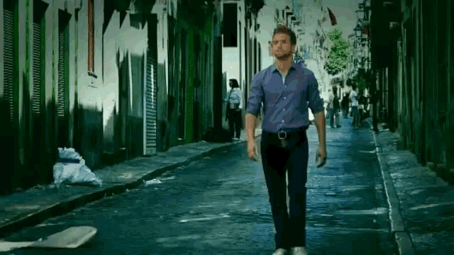 a man in a blue shirt walks down a narrow street