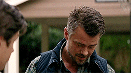 a man with a beard and a vest is standing in front of a house .