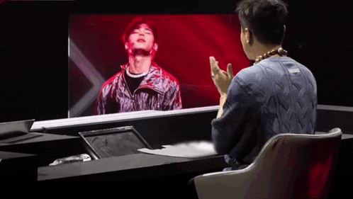 a man sitting in front of a screen with a picture of a man in a red jacket on it