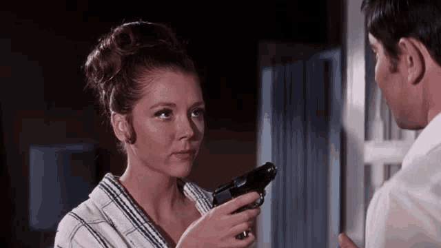 a woman in a bathrobe is holding a gun to a man