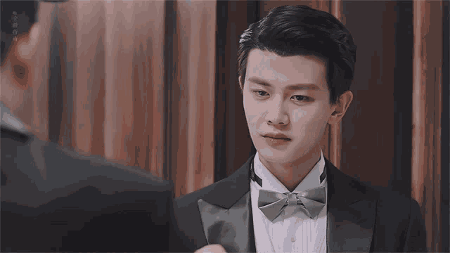 a man in a tuxedo with a bow tie is looking at another man