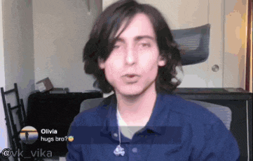 a young man with long hair is sitting in a chair in a room talking to someone .