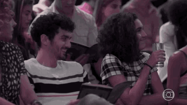 a man and a woman are sitting in a crowd with a woman holding a glass of water .