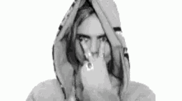 a black and white photo of a woman wearing a hooded sweatshirt pointing at the camera .