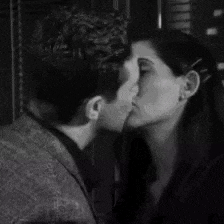 a man and a woman are kissing in front of a window in a black and white photo .