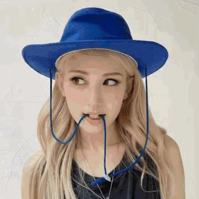 a woman wearing a blue cowboy hat with a string coming out of her mouth .