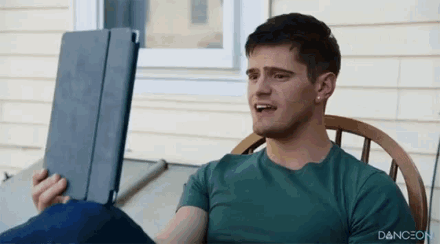 a man in a green shirt is sitting in a chair holding a tablet with the word dance on the bottom right