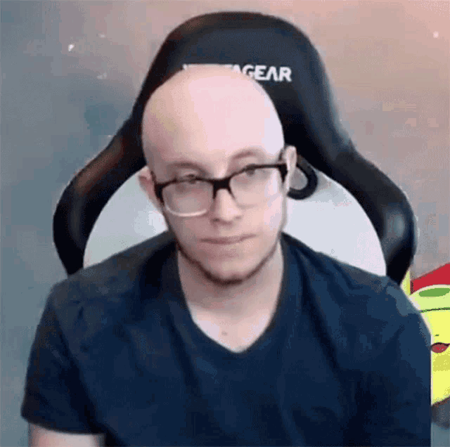 a bald man wearing glasses and a blue shirt is sitting in a chair .
