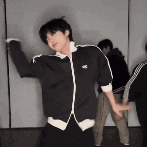 a man in a black adidas jacket is dancing in front of a group of people