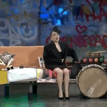 a woman is sitting on a bench next to a drum in front of a graffiti wall .