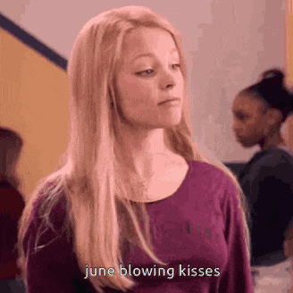 a girl in a purple shirt is blowing kisses in a hallway .