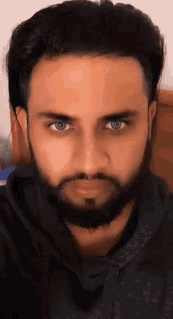 a man with a beard and blue eyes is wearing a black hoodie