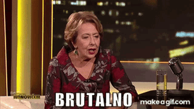 a woman is sitting at a table with a microphone and the word brutalno written on the screen