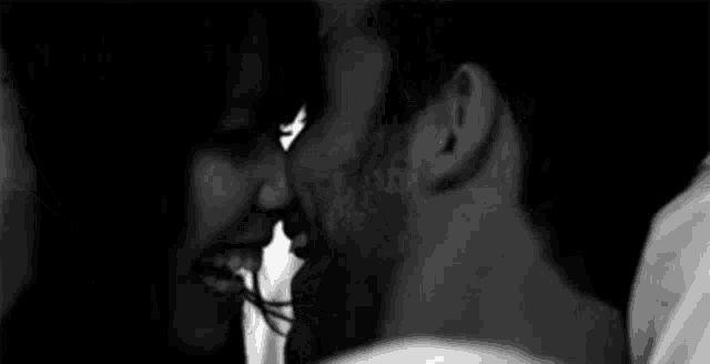 a black and white photo of a man and a woman kissing .