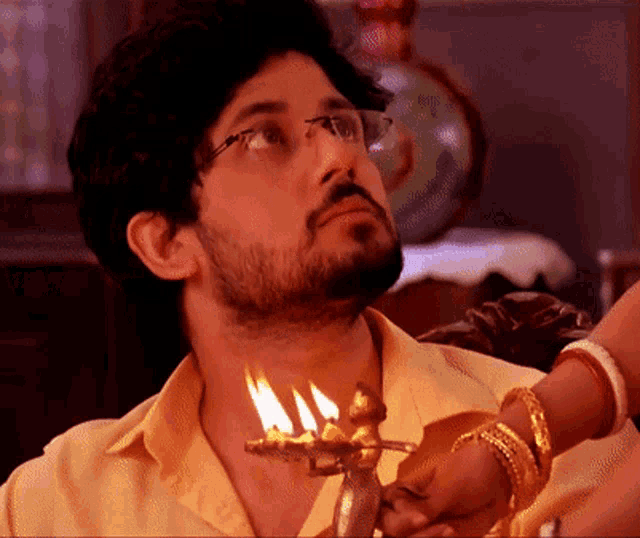 a man with a beard and glasses holds a candle in his hand