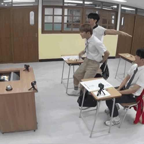 a group of boys are sitting at desks in a classroom and one of them is pointing