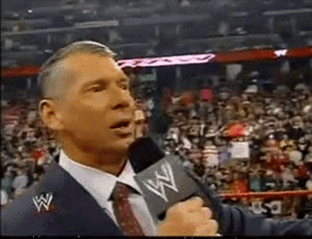 a man in a suit is talking into a microphone with a w logo on his jacket
