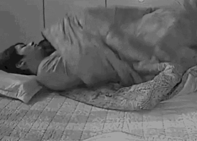 a black and white photo of a woman laying on a bed with a dog .