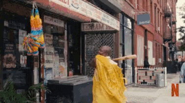a man in a yellow cape is holding a bat in front of a store .