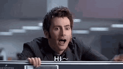 a man in a suit is standing behind a desk with his mouth open and saying hi .