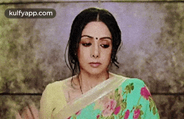 a woman in a floral saree is making a funny face with her hands .