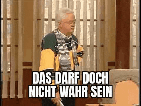 a man is standing in front of a computer in an office with a sign that says `` das darf doch nicht wahr sein ''
