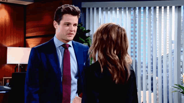 a man in a suit and tie stands next to a woman in a black suit