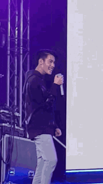 a man is holding a microphone and smiling while standing on a stage