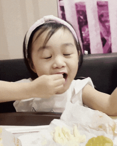 a little girl wearing a pink headband is eating a hamburger