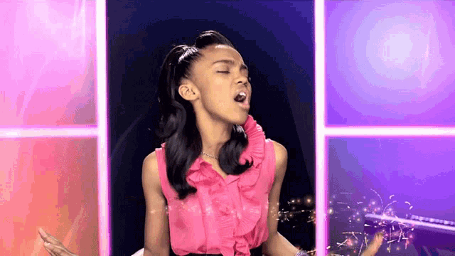 a girl in a pink ruffled top is singing with her eyes closed