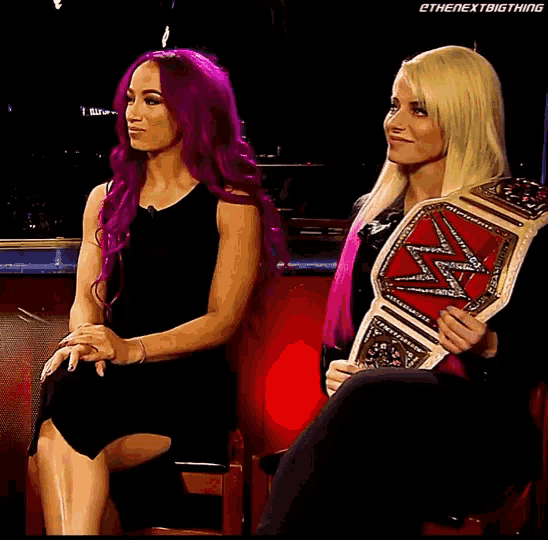 two women are sitting next to each other and one is holding a wwe championship belt