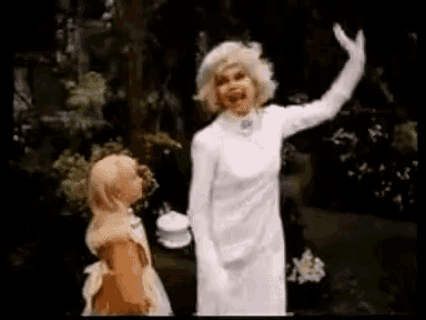 a woman in a white dress is waving at a little girl .