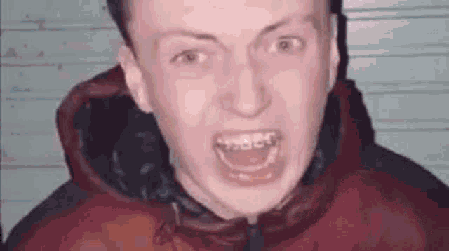 a young man in a red jacket is making a funny face with his mouth open .