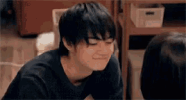 a young man is making a funny face while sitting in front of a woman .