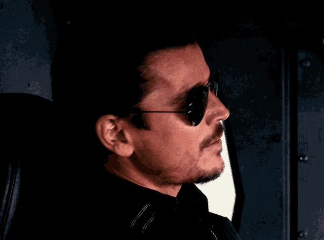 a man wearing sunglasses and a black jacket smiles