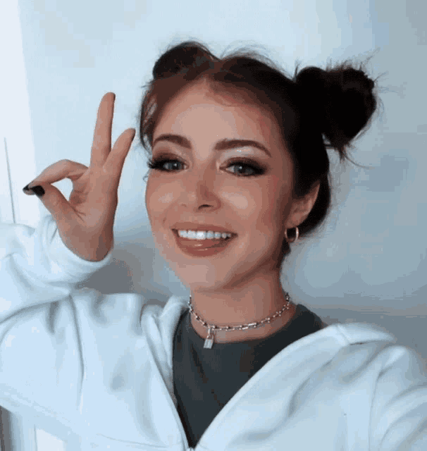 a woman wearing a choker necklace and a white hoodie giving the ok sign