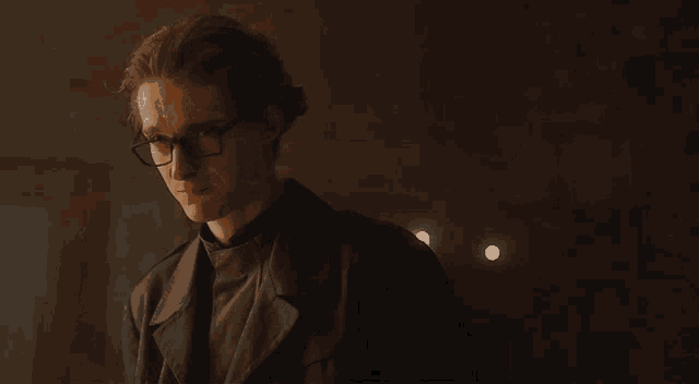 a man wearing glasses and a black coat looks down at something