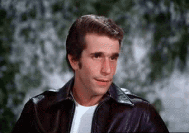 a man in a leather jacket and white shirt is smiling .