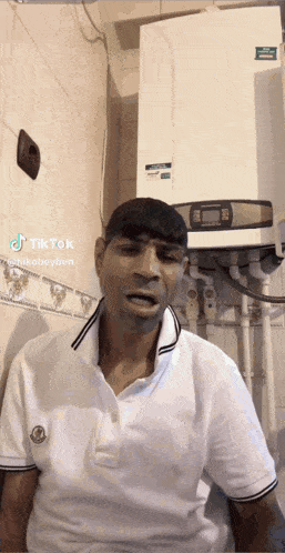 a man in a white shirt is standing in front of a wall with a heater on it