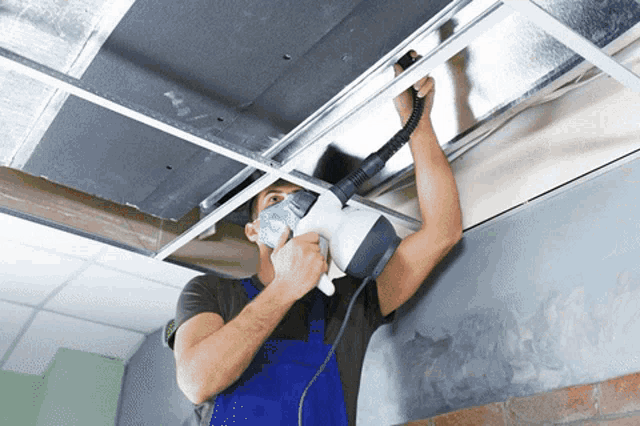a man wearing a mask is using a vacuum cleaner to clean a ceiling
