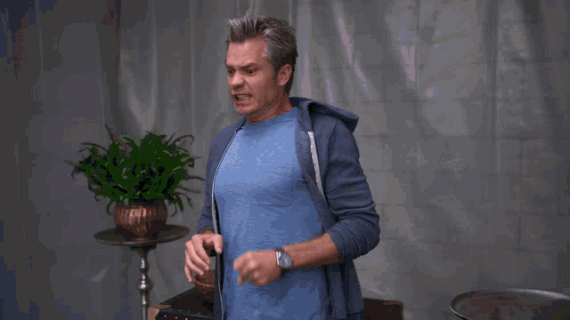 a man in a blue shirt is standing in front of a white curtain that says " okay "