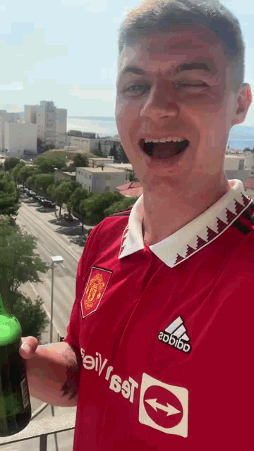 a man wearing a red adidas shirt is holding a bottle