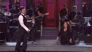 a man in a tuxedo is dancing on a stage with a band