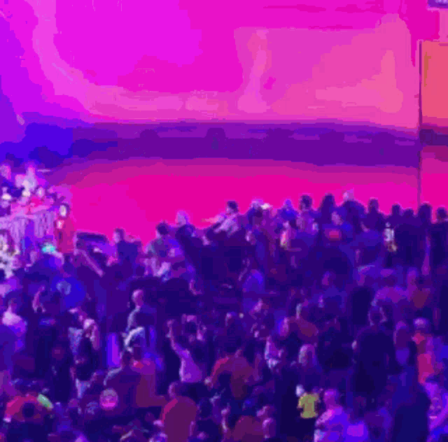 a crowd of people gathered in front of a stage with purple lights