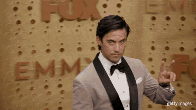 a man in a tuxedo giving a peace sign in front of fox emmy awards