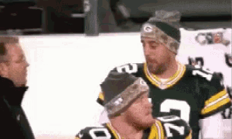 a man wearing a green bay packers jersey talks to two other men