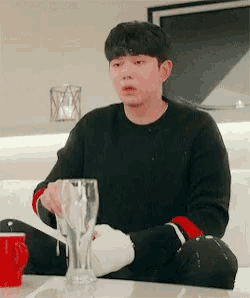 a man in a black sweater is sitting at a table holding a glass of beer