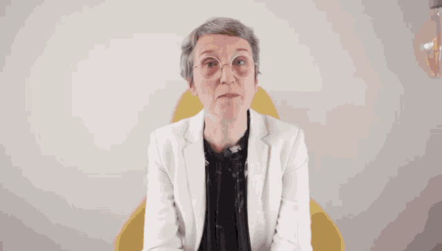 a woman wearing glasses and a white jacket says bah salut