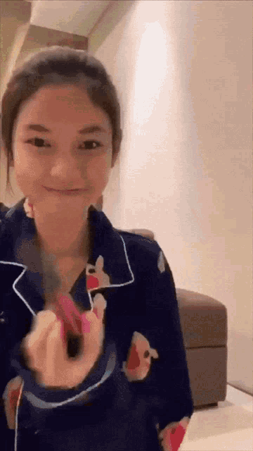 a woman wearing a blue pajama top is smiling and holding a pink object