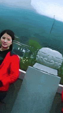 a woman in a red jacket stands next to a statue of a face